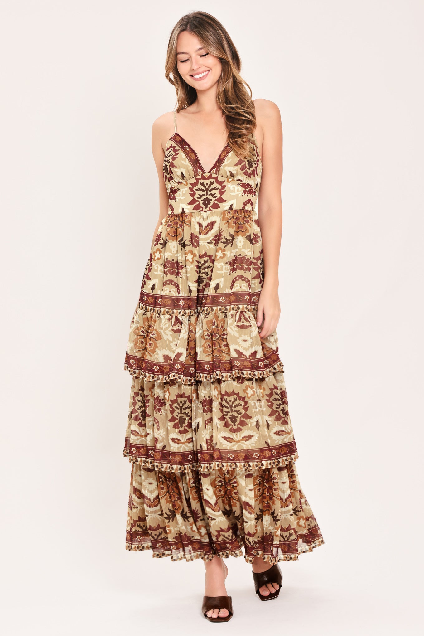 A woman modeling a sleeveless, tiered maxi dress with a bohemian-style floral and geometric pattern in brown and beige | Flying Tomato
