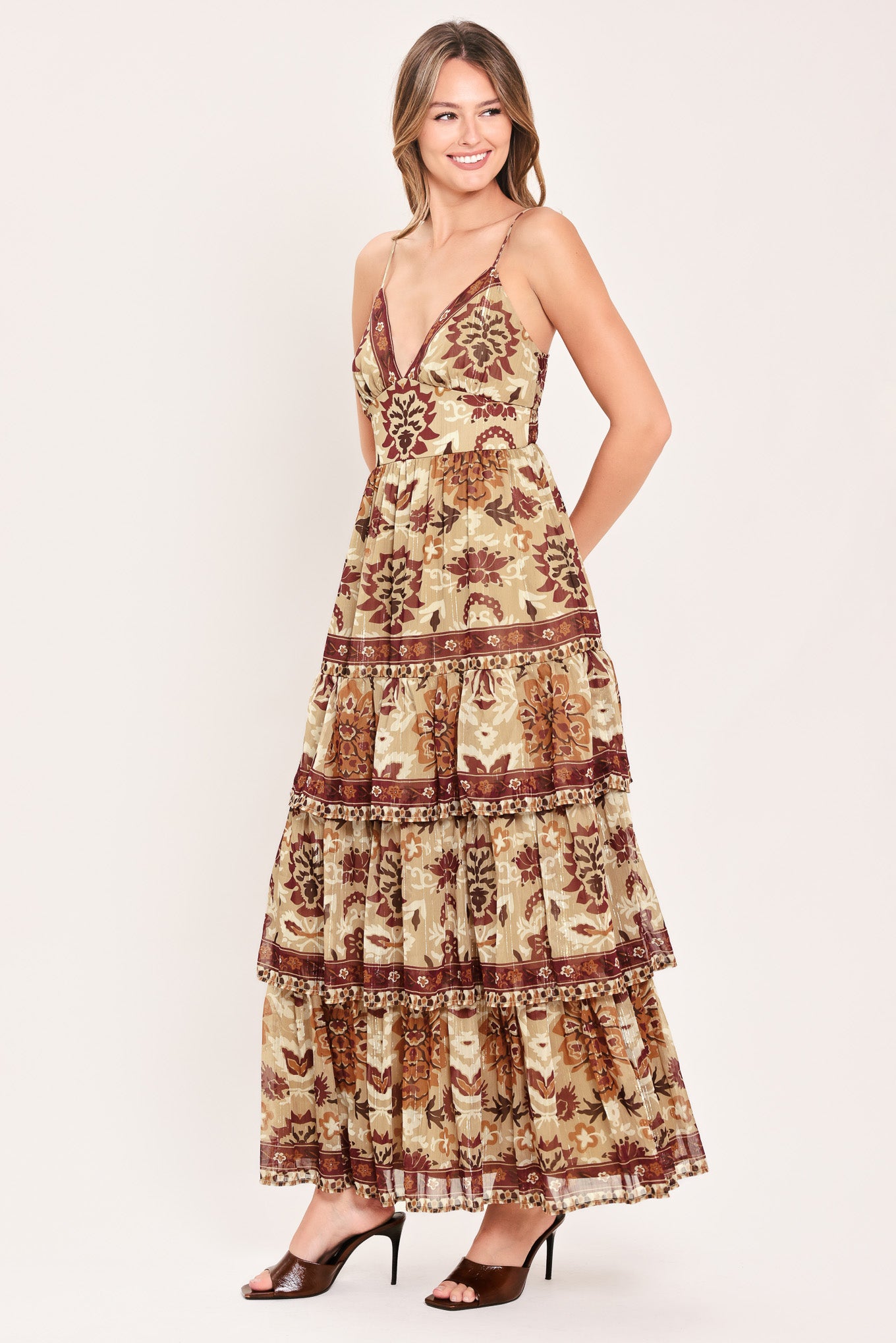 A woman modeling a sleeveless, tiered maxi dress with a bohemian-style floral and geometric pattern in brown and beige | Flying Tomato