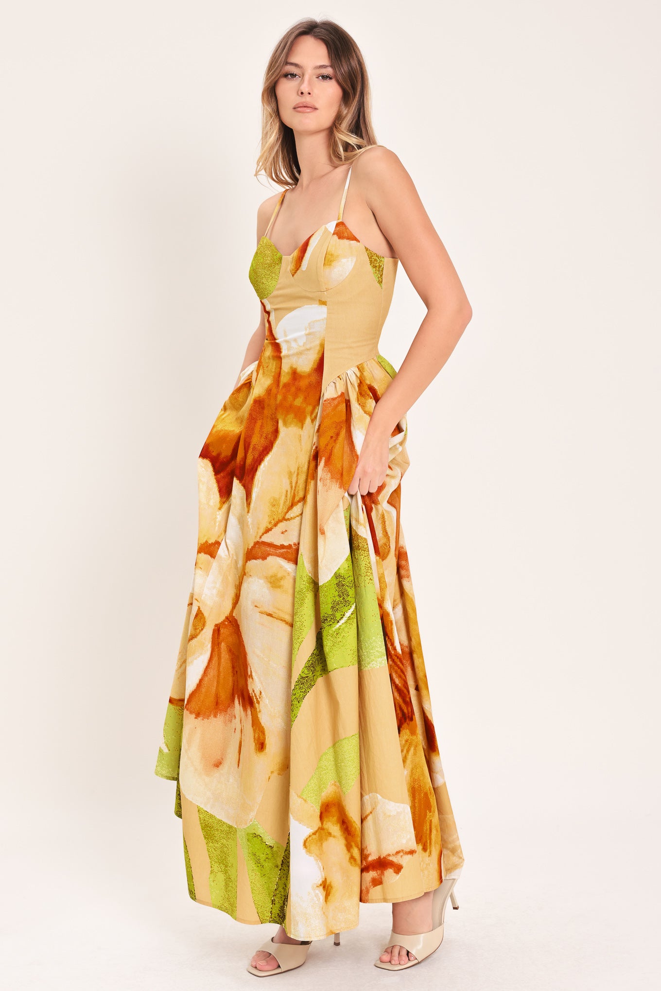 Woman wearing a green with brown and khaki floral printed maxi dress featuring bustier top, straps, side shirring detail and back zipper closure | Flying Tomato
