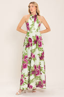 Woman wearing an ivory maxi dress with purple and green floral pattern featuring a halter neckline with collared finish, front button detail, full skirt, bare back with zipper closure | Flying Tomato