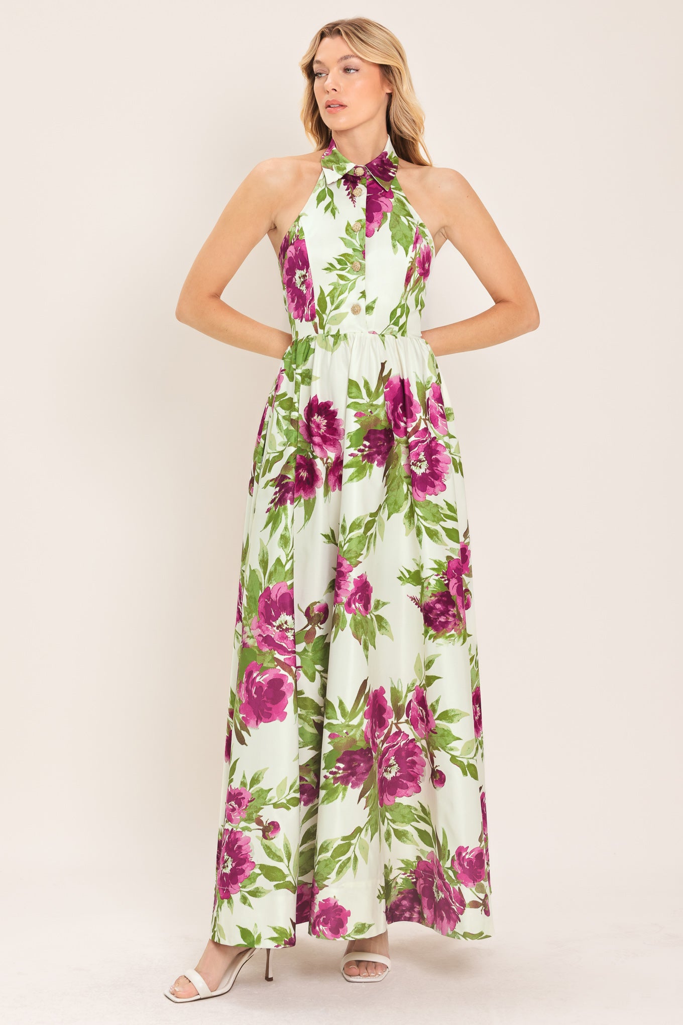 Woman wearing an ivory maxi dress with purple and green floral pattern featuring a halter neckline with collared finish, front button detail, full skirt, bare back with zipper closure | Flying Tomato