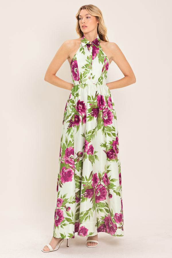 Woman wearing an ivory maxi dress with purple and green floral pattern featuring a halter neckline with collared finish, front button detail, full skirt, bare back with zipper closure | Flying Tomato