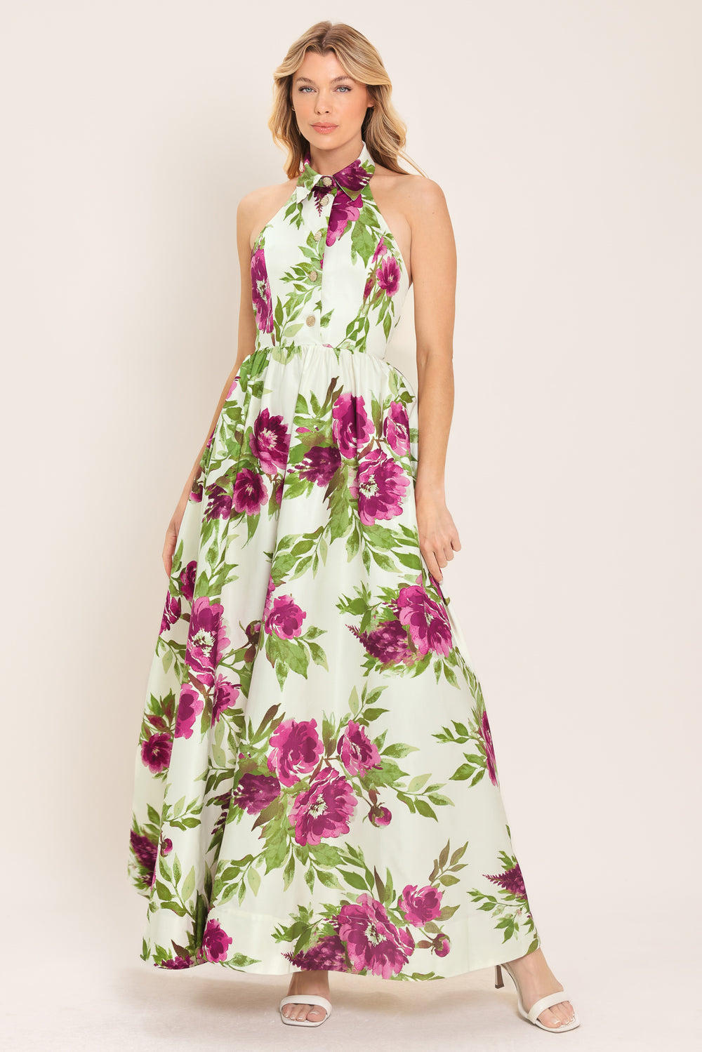 Woman wearing an ivory maxi dress with purple and green floral pattern featuring a halter neckline with collared finish, front button detail, full skirt, bare back with zipper closure | Flying Tomato
