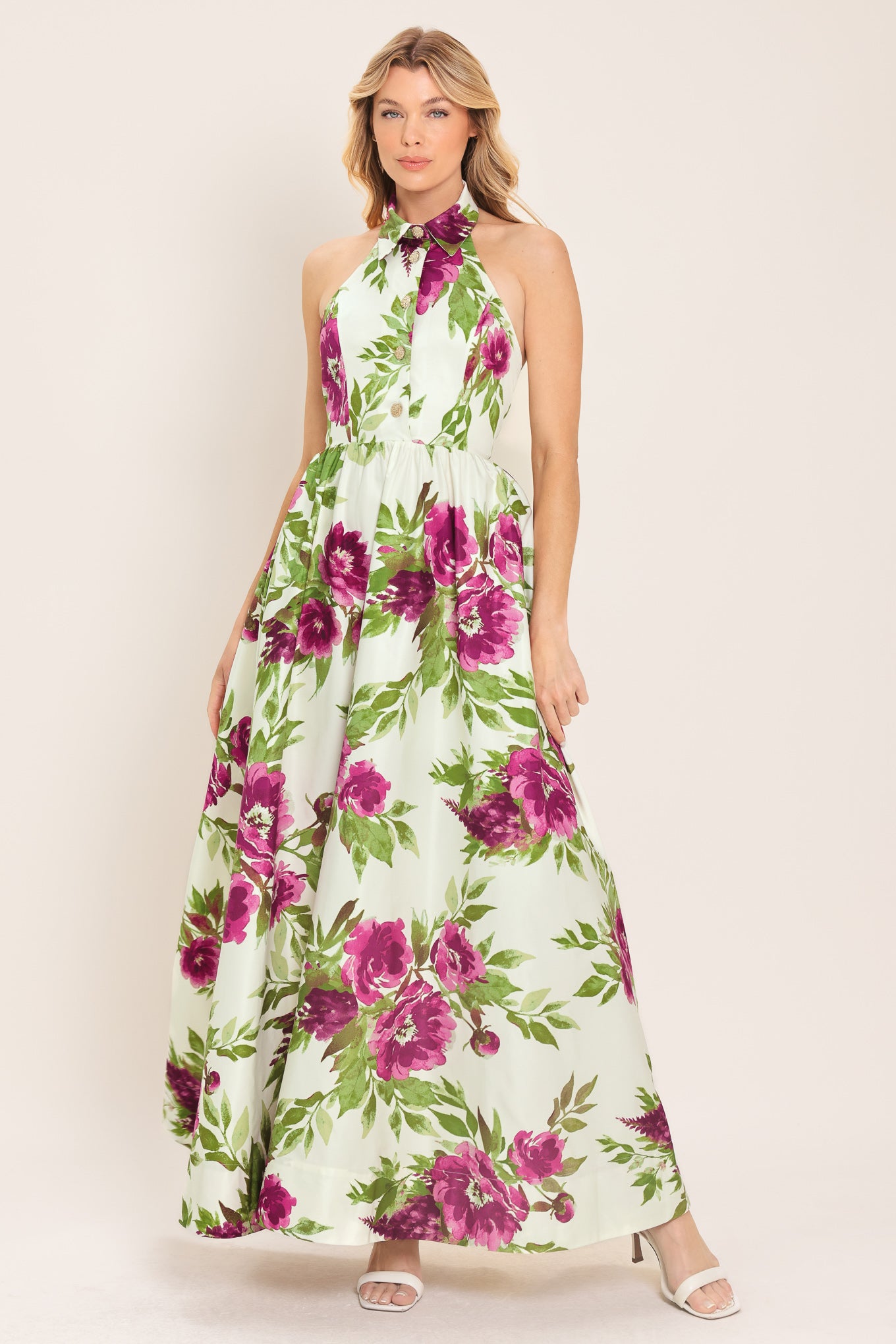 Woman wearing an ivory maxi dress with purple and green floral pattern featuring a halter neckline with collared finish, front button detail, full skirt, bare back with zipper closure | Flying Tomato