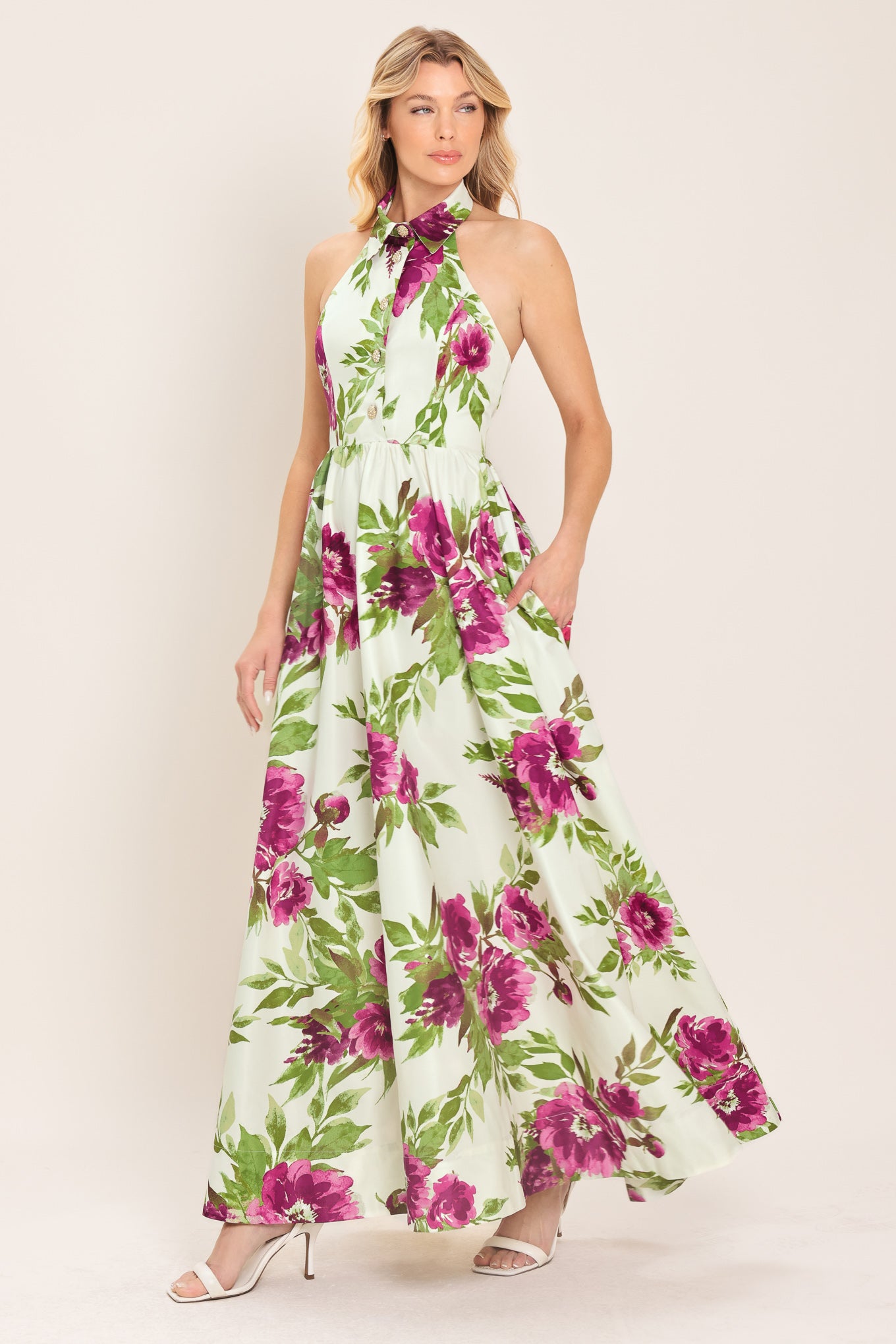 Woman wearing an ivory maxi dress with purple and green floral pattern featuring a halter neckline with collared finish, front button detail, full skirt, bare back with zipper closure | Flying Tomato