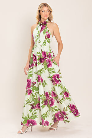 Woman wearing an ivory maxi dress with purple and green floral pattern featuring a halter neckline with collared finish, front button detail, full skirt, bare back with zipper closure | Flying Tomato