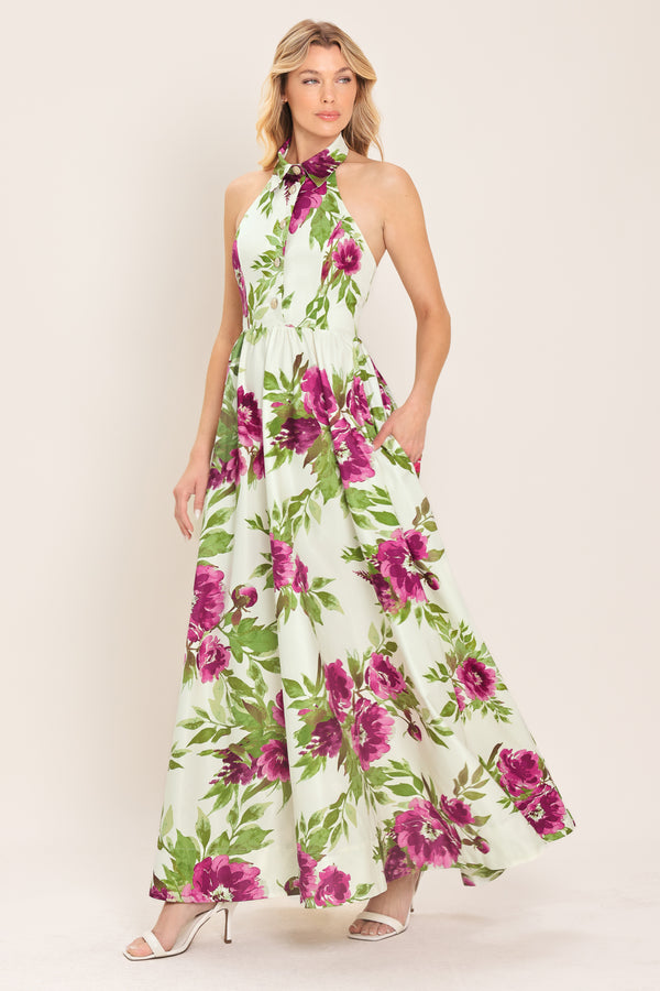 Woman wearing an ivory maxi dress with purple and green floral pattern featuring a halter neckline with collared finish, front button detail, full skirt, bare back with zipper closure | Flying Tomato