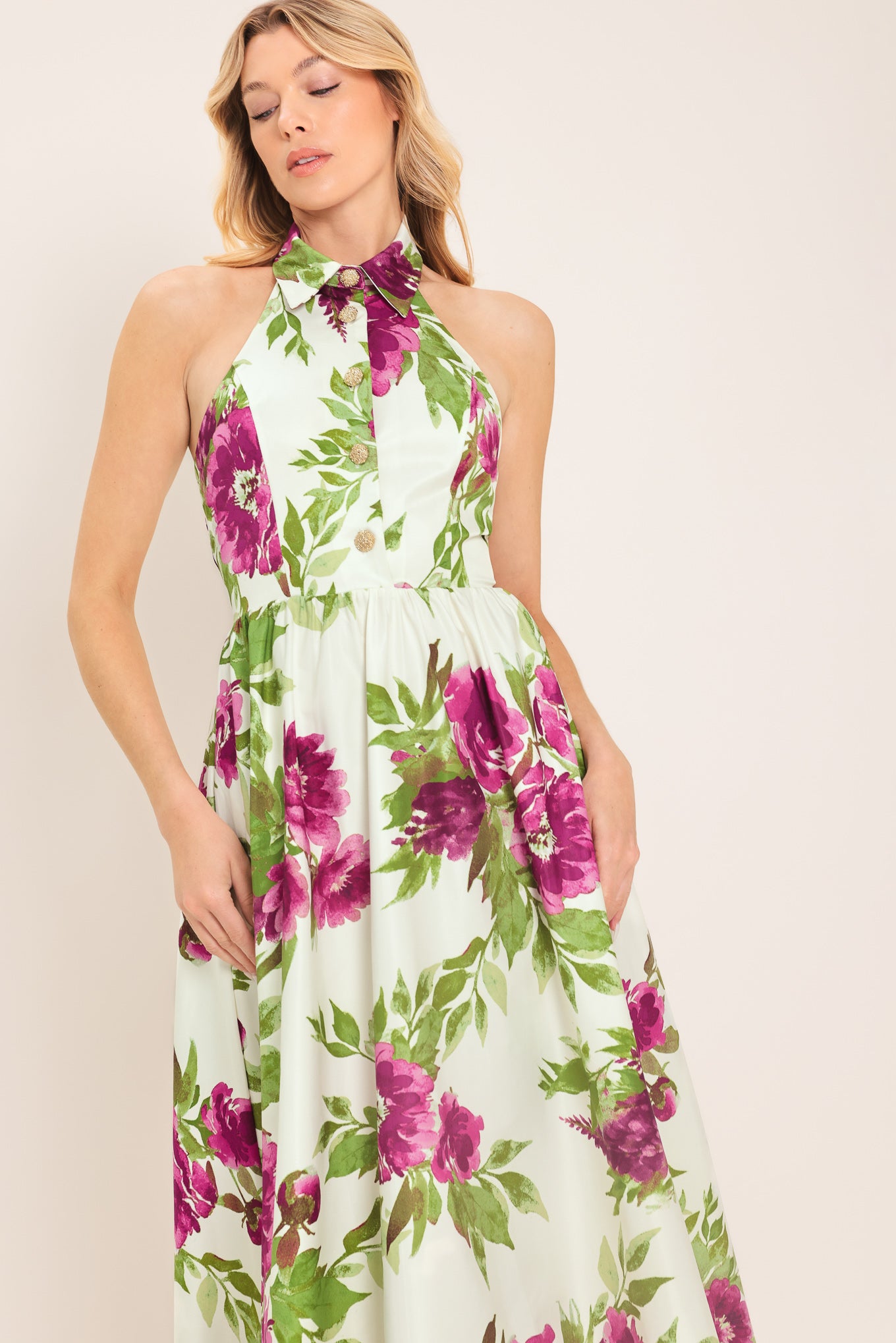 Woman wearing an ivory maxi dress with purple and green floral pattern featuring a halter neckline with collared finish, front button detail, full skirt, bare back with zipper closure | Flying Tomato