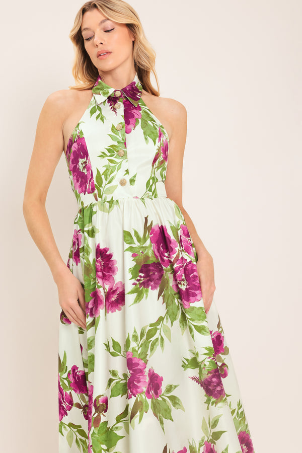 Woman wearing an ivory maxi dress with purple and green floral pattern featuring a halter neckline with collared finish, front button detail, full skirt, bare back with zipper closure | Flying Tomato