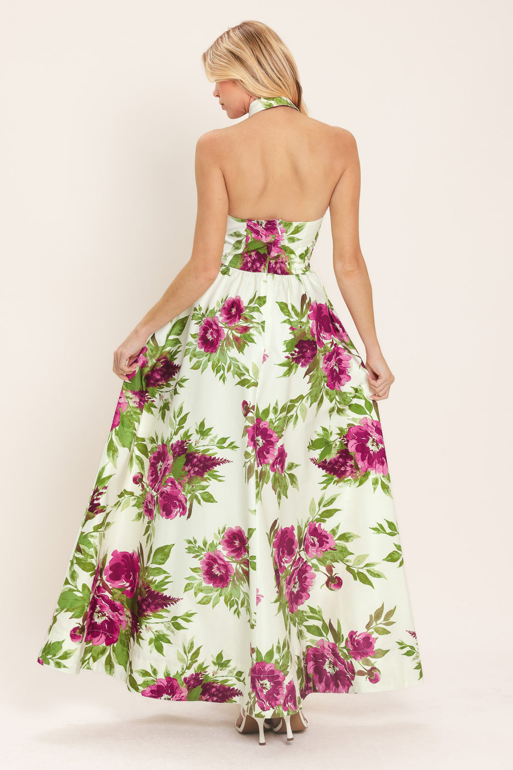 Woman wearing an ivory maxi dress with purple and green floral pattern featuring a halter neckline with collared finish, front button detail, full skirt, bare back with zipper closure | Flying Tomato