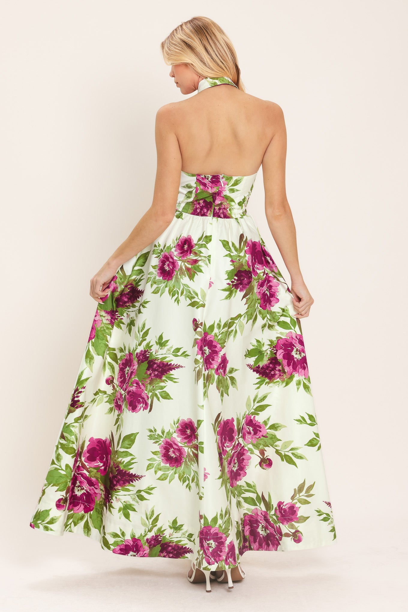 Woman wearing an ivory maxi dress with purple and green floral pattern featuring a halter neckline with collared finish, front button detail, full skirt, bare back with zipper closure | Flying Tomato