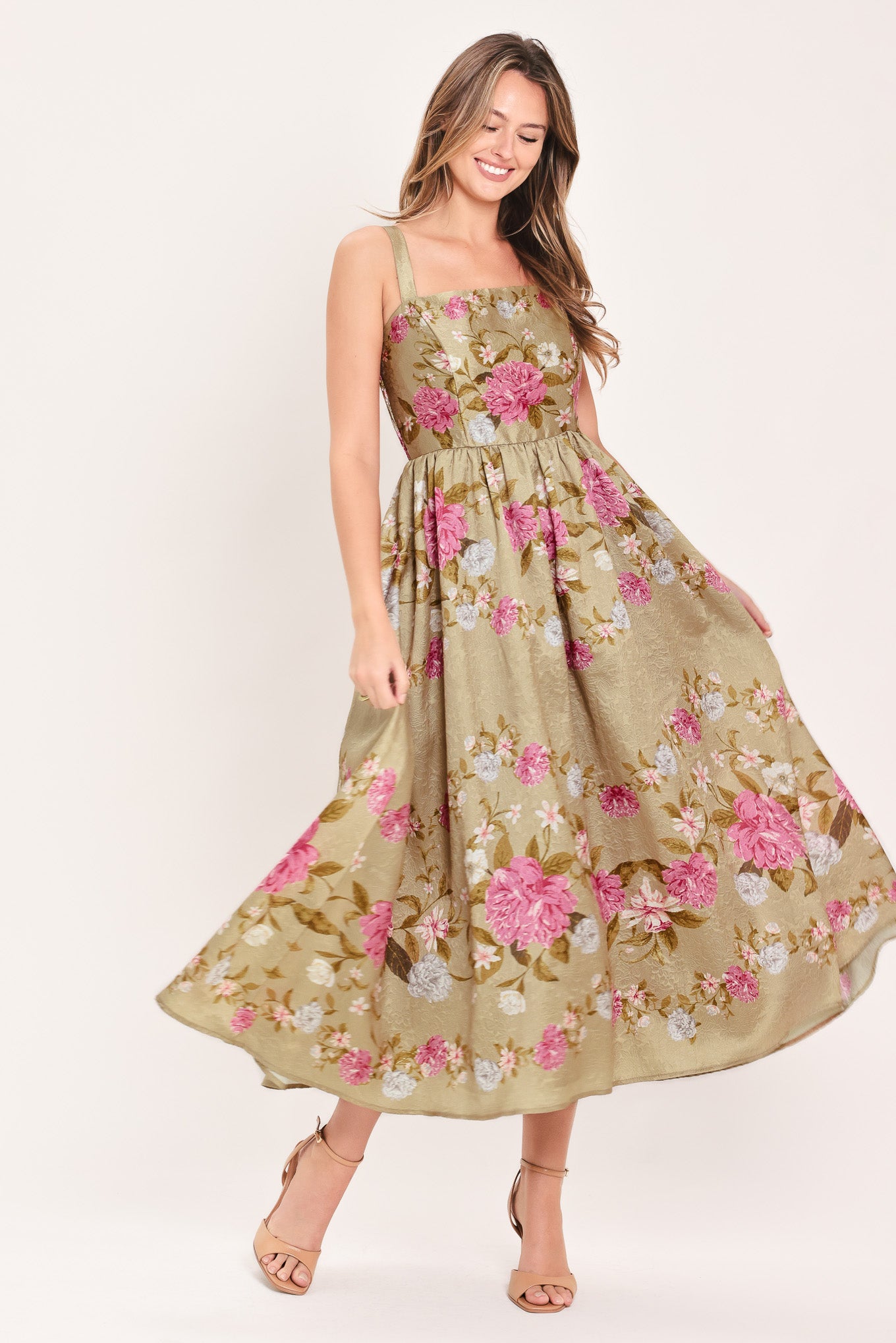A woman wearing a sleeveless midi dress with a floral print on tan background. The dress features pink, white, and yellow flowers with green leaves | Flying Tomato