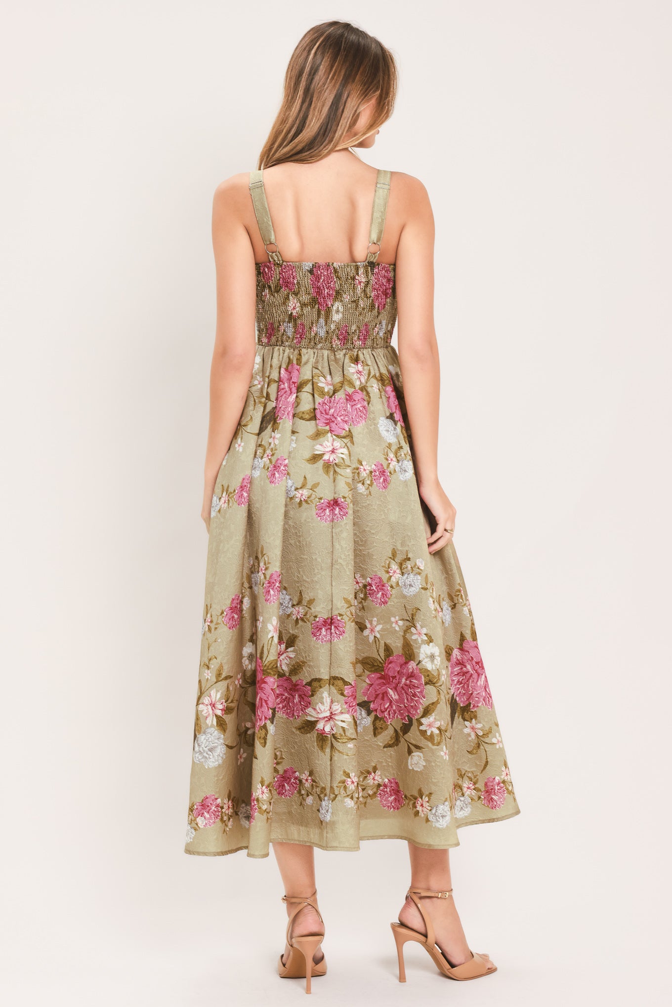 A woman wearing a sleeveless midi dress with a floral print on tan background. The dress features pink, white, and yellow flowers with green leaves | Flying Tomato