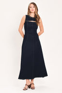 A woman wearing a sleeveless dark navy maxi dress with a crew neckline, a horizontal cutout across the chest, and small gold stud embellishments | Flying Tomato
