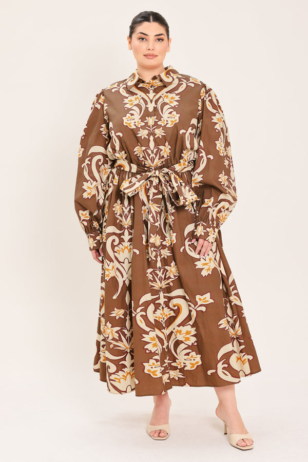 A woman modeling a brown long-sleeve midi dress with a cream and gold baroque-style floral pattern, featuring a tie waist belt and a shawl collar | Plus Curve Flying Tomato