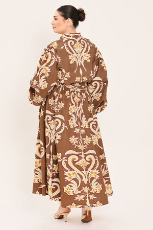 A woman modeling a brown long-sleeve midi dress with a cream and gold baroque-style floral pattern, featuring a tie waist belt and a shawl collar | Plus Curve Flying Tomato