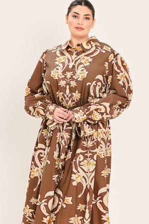 A woman modeling a brown long-sleeve midi dress with a cream and gold baroque-style floral pattern, featuring a tie waist belt and a shawl collar | Plus Curve Flying Tomato