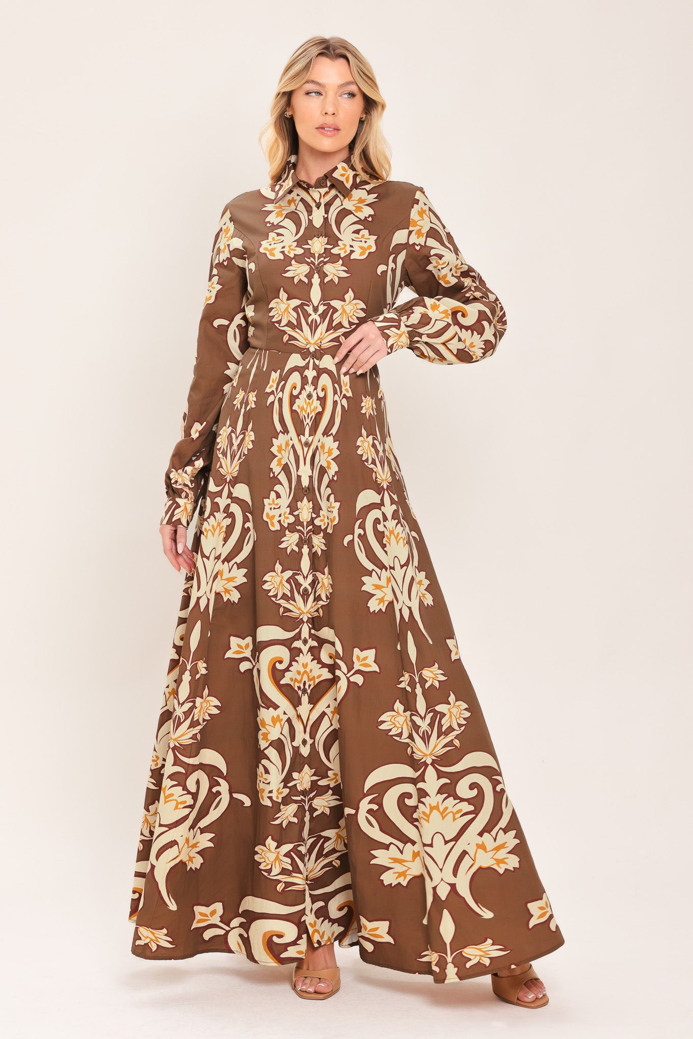 A woman wearing a long-sleeve, high-neck button up maxi dress with a brown base and a beige and gold baroque-style floral pattern | Flying Tomato