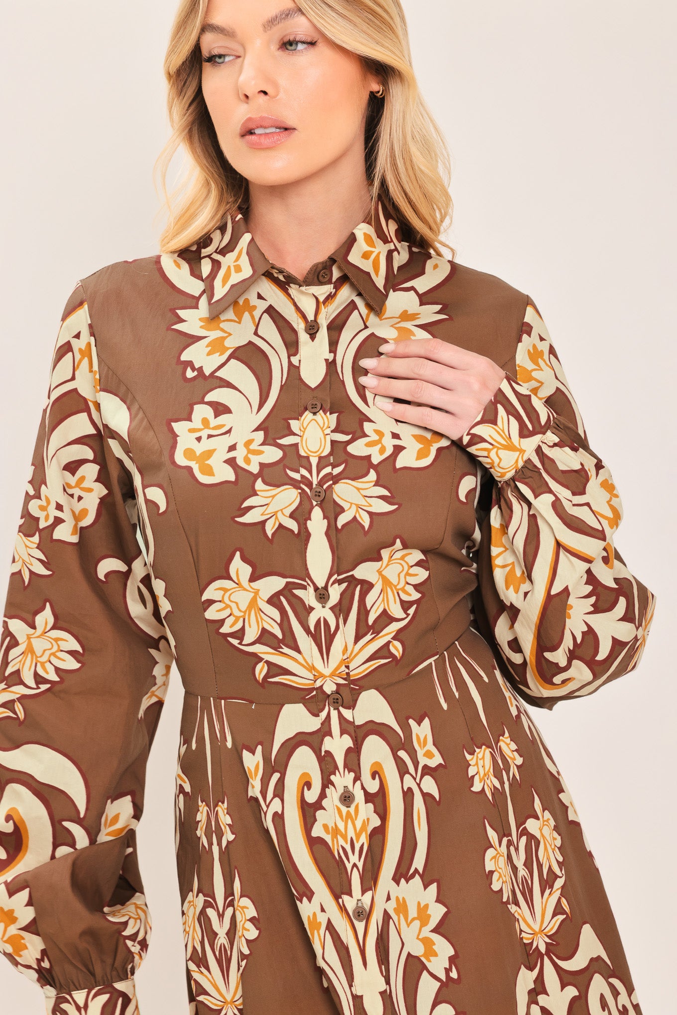 A woman wearing a long-sleeve, high-neck button up maxi dress with a brown base and a beige and gold baroque-style floral pattern | Flying Tomato