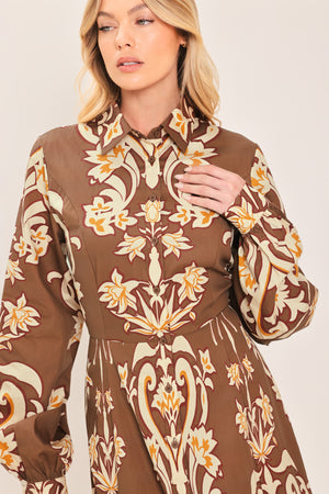 A woman wearing a long-sleeve, high-neck button up maxi dress with a brown base and a beige and gold baroque-style floral pattern | Flying Tomato