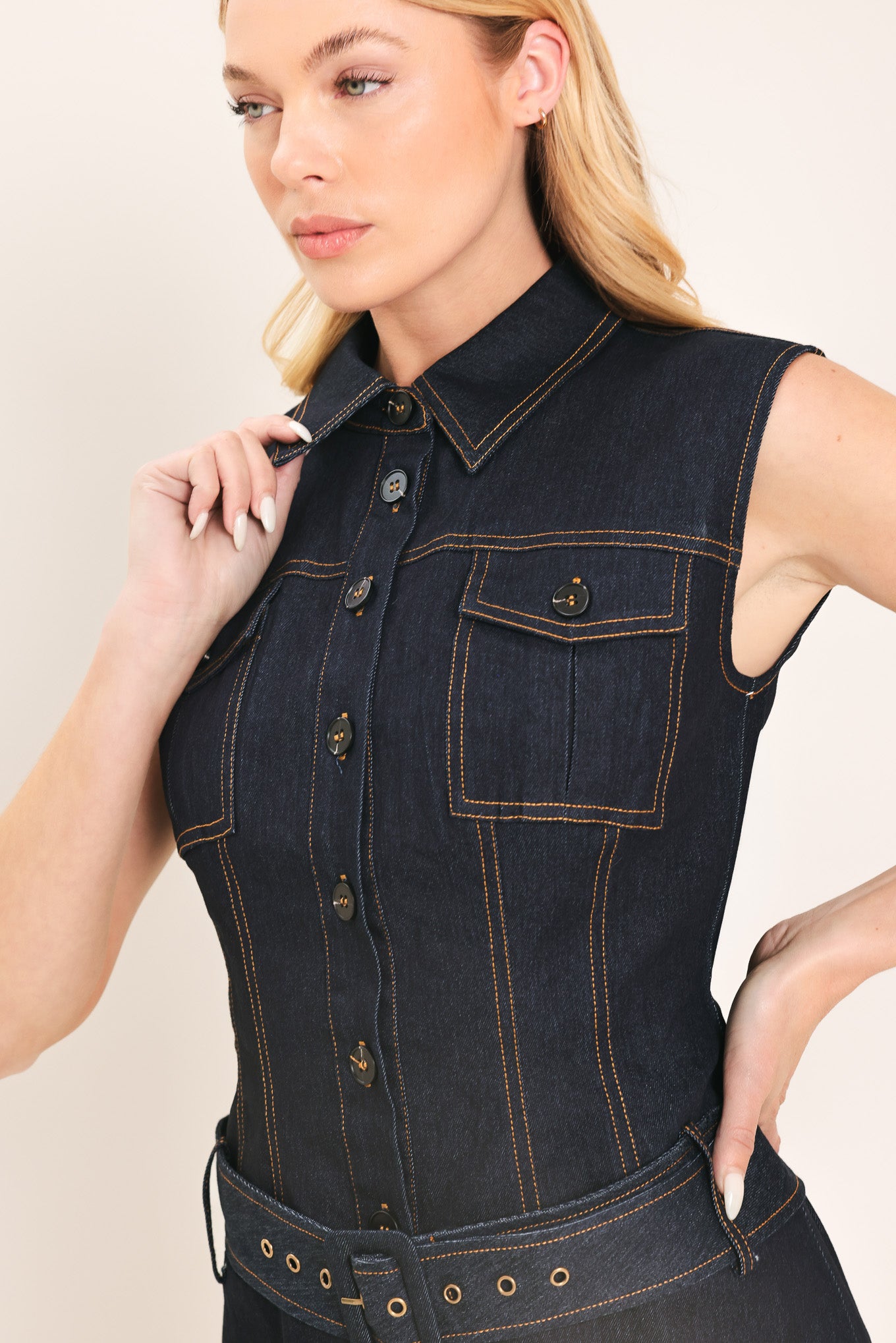 Woman wearing a sleeveless dark denim mini dress featuring collar, front button down and drop waist with belt | Flying Tomato