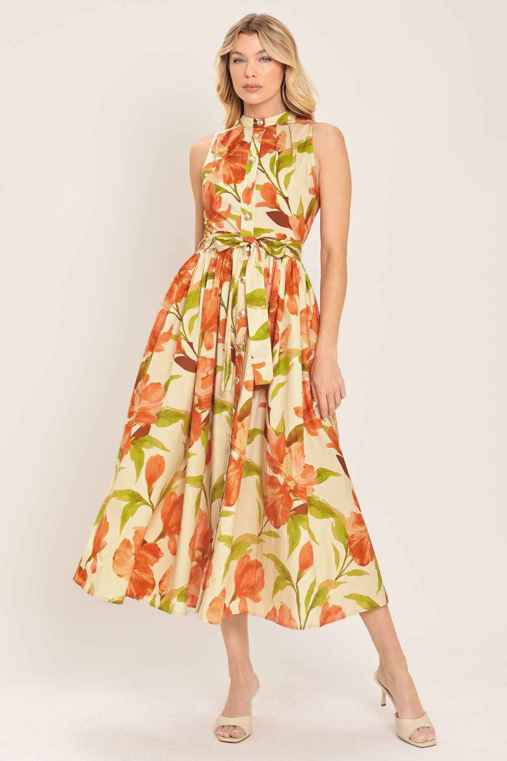 Woman wearing a sleeveless ivory and apricot floral midi dress featuring band collar, button down, self sash tie and full skirt | Flying Tomato