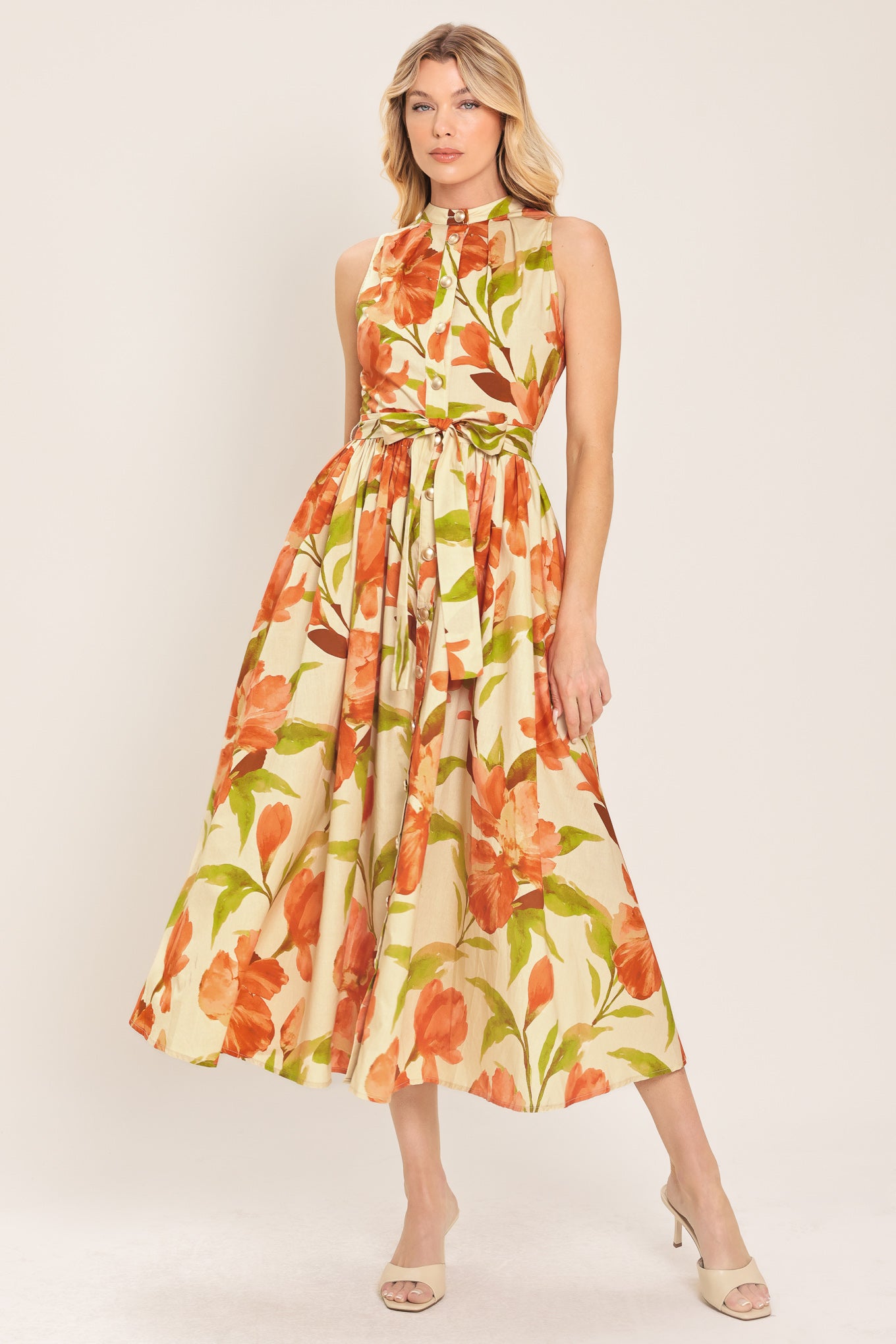 Woman wearing a sleeveless ivory and apricot floral midi dress featuring band collar, button down, self sash tie and full skirt | Flying Tomato