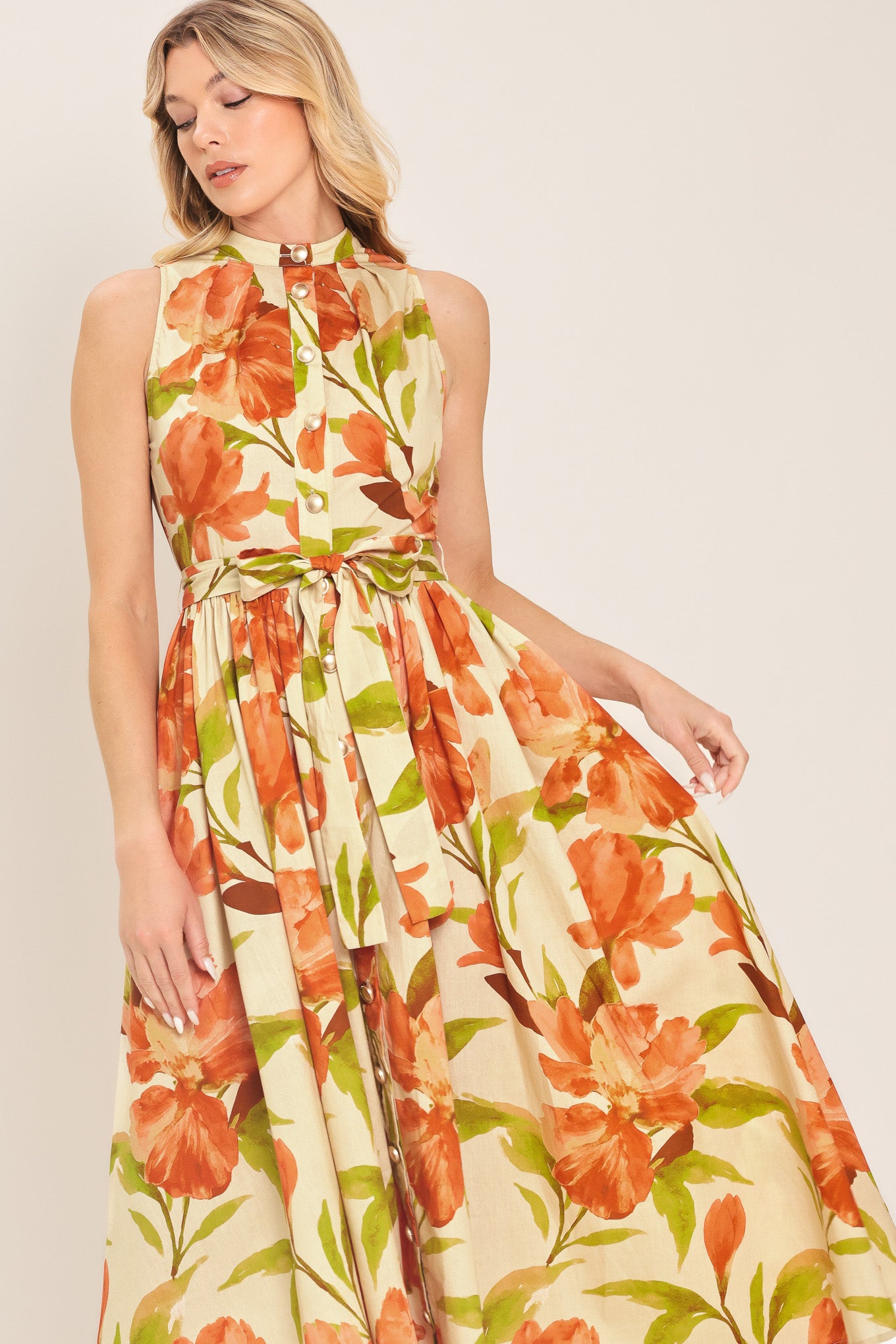 Woman wearing a sleeveless ivory and apricot floral midi dress featuring band collar, button down, self sash tie and full skirt | Flying Tomato