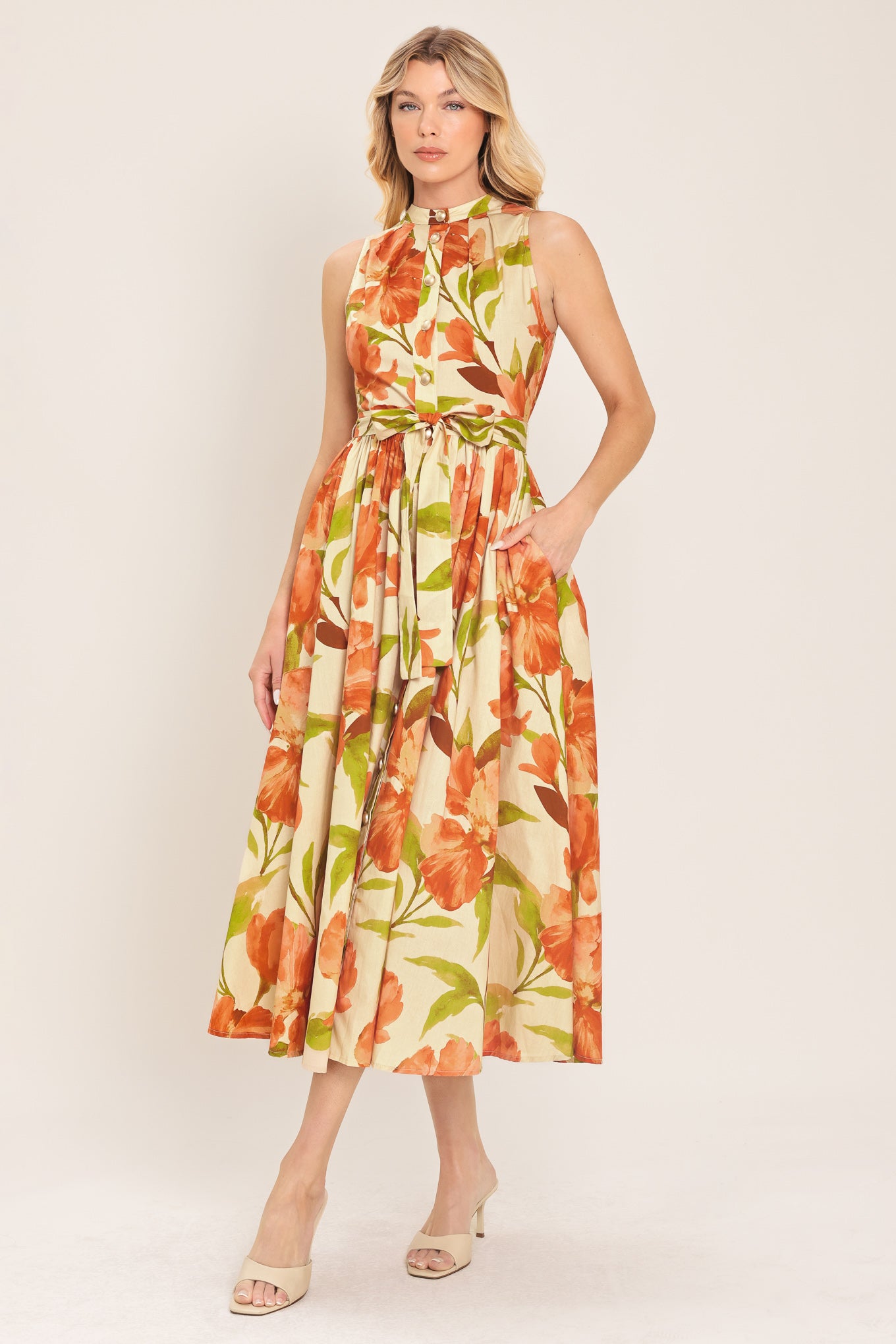 Woman wearing a sleeveless ivory and apricot floral midi dress featuring band collar, button down, self sash tie and full skirt | Flying Tomato