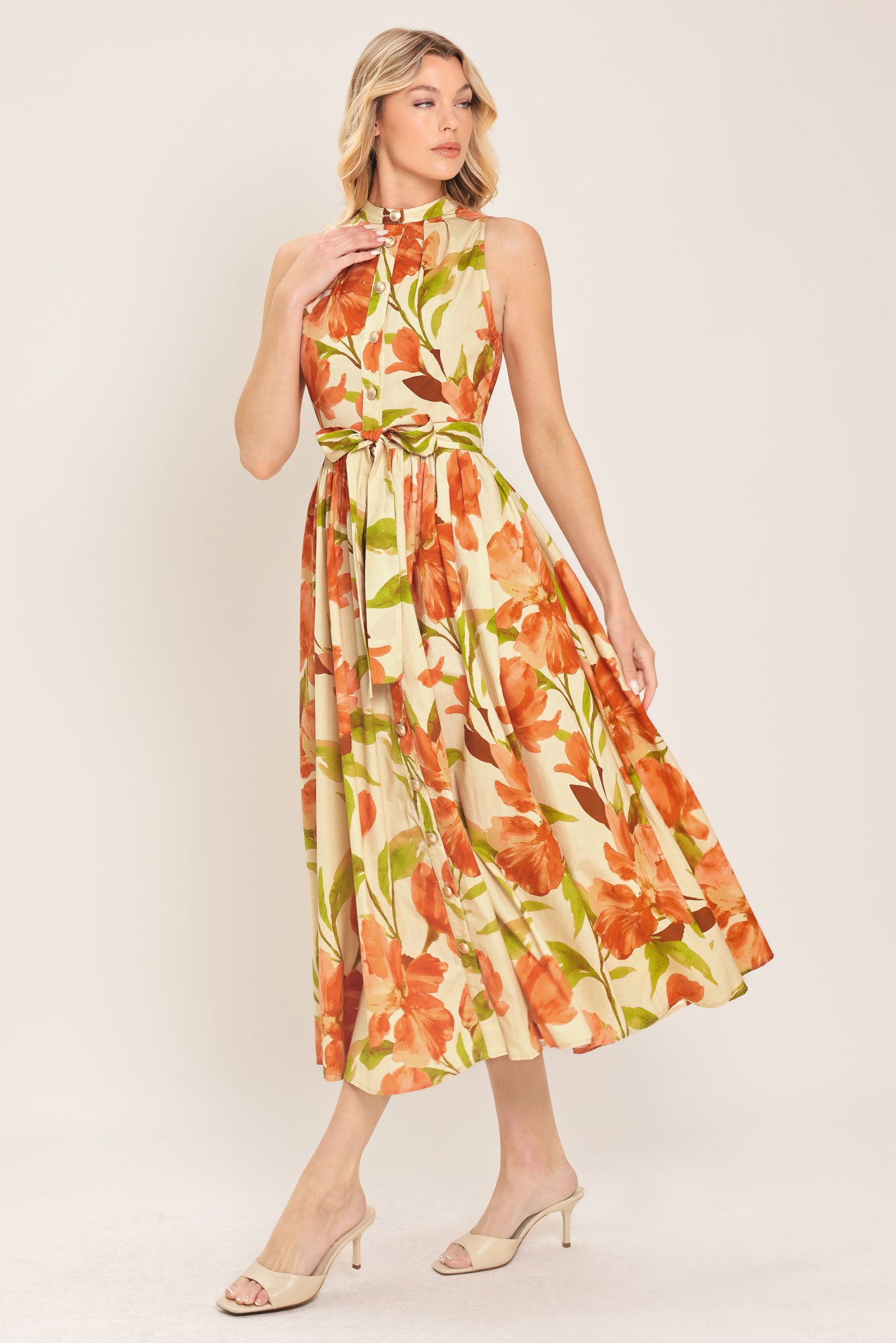 Woman wearing a sleeveless ivory and apricot floral midi dress featuring band collar, button down, self sash tie and full skirt | Flying Tomato