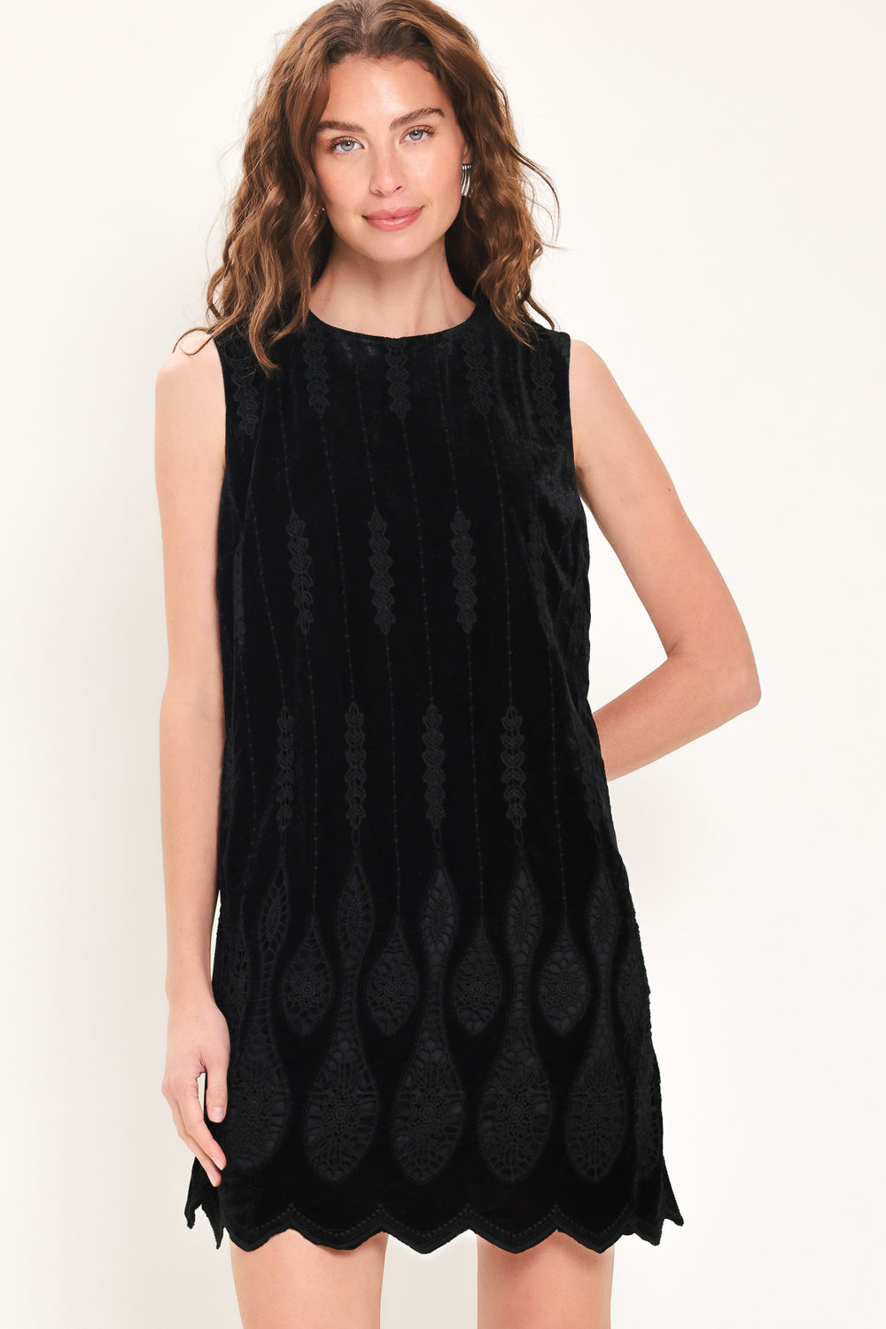 A woman wearing a sleeveless black velvet mini dress with a textured design and wavy hemline | Flying Tomato