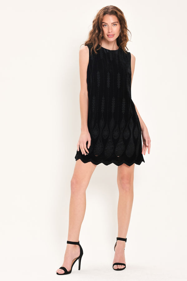 A woman wearing a sleeveless black velvet mini dress with a textured design and wavy hemline | Flying Tomato
