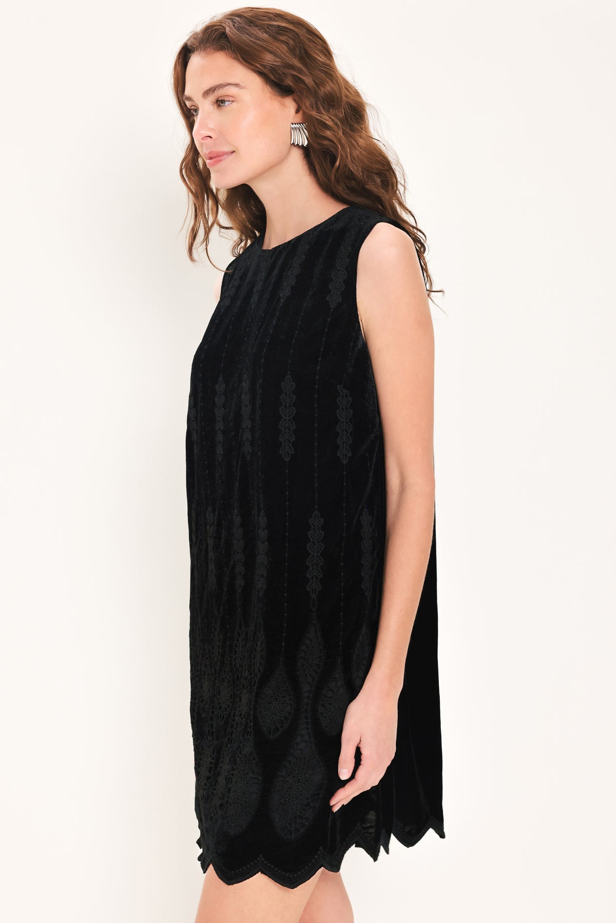 A woman wearing a sleeveless black velvet mini dress with a textured design and wavy hemline | Flying Tomato