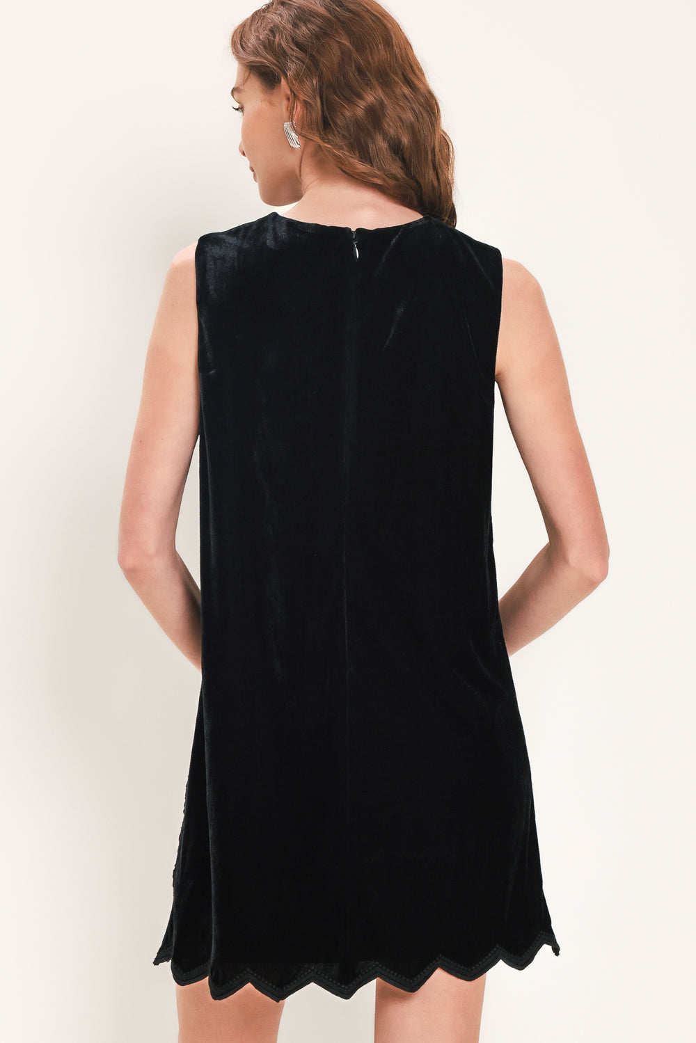 A woman wearing a sleeveless black velvet mini dress with a textured design and wavy hemline | Flying Tomato