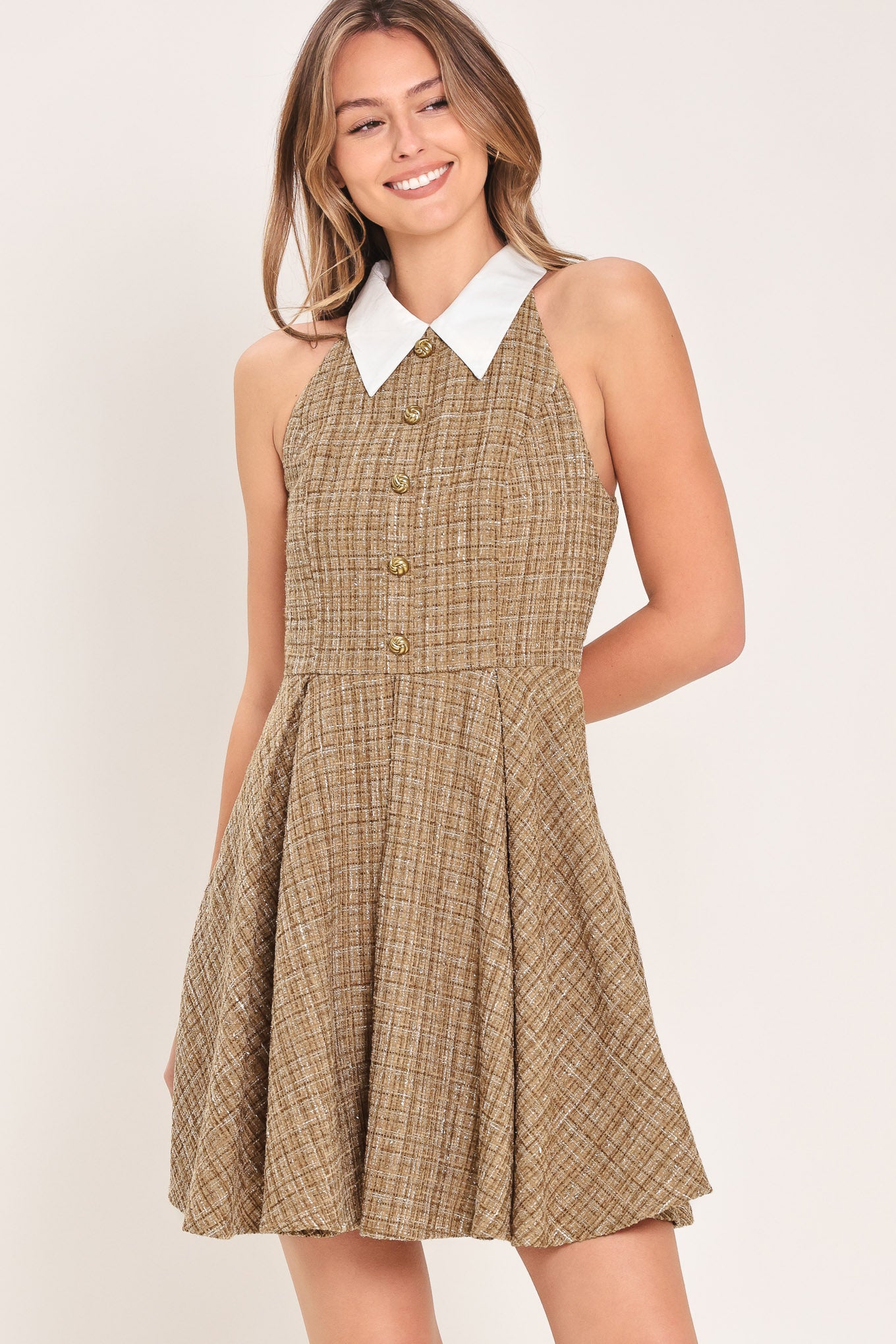 Woman wearing a hazel tweed mini dress featuring halter neckline with white collar finish, front button detail, full circle skirt and back zipper closure background | Flying Tomato