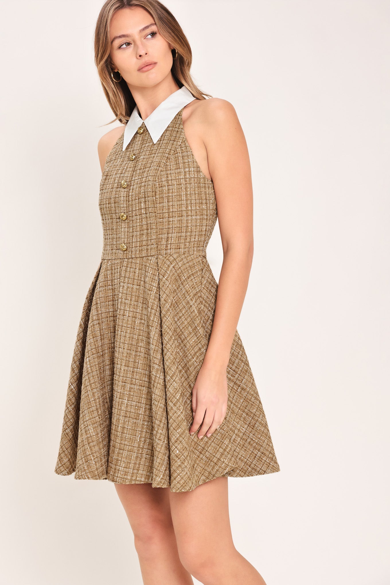 Woman wearing a hazel tweed mini dress featuring halter neckline with white collar finish, front button detail, full circle skirt and back zipper closure background | Flying Tomato