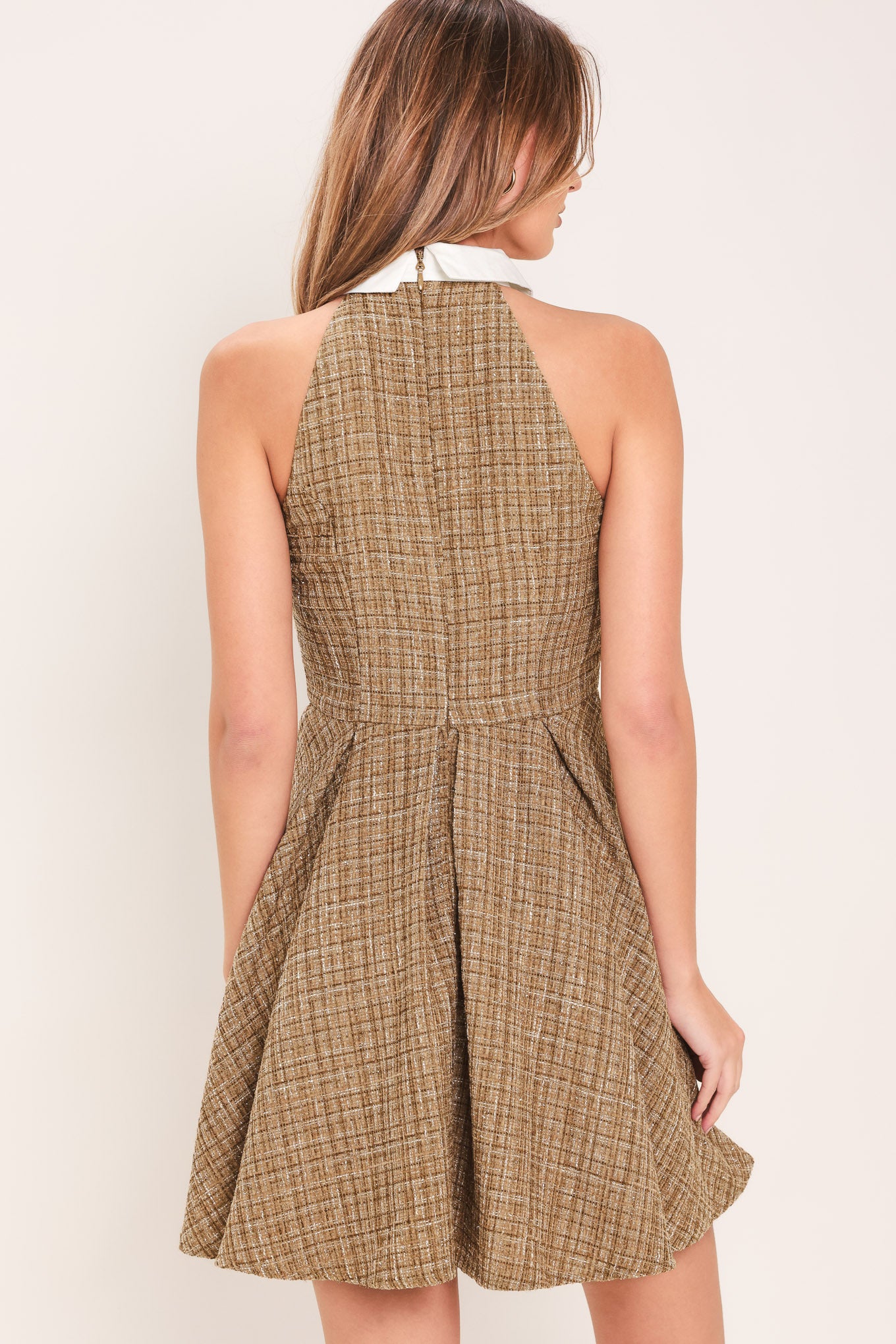 Woman wearing a hazel tweed mini dress featuring halter neckline with white collar finish, front button detail, full circle skirt and back zipper closure background | Flying Tomato