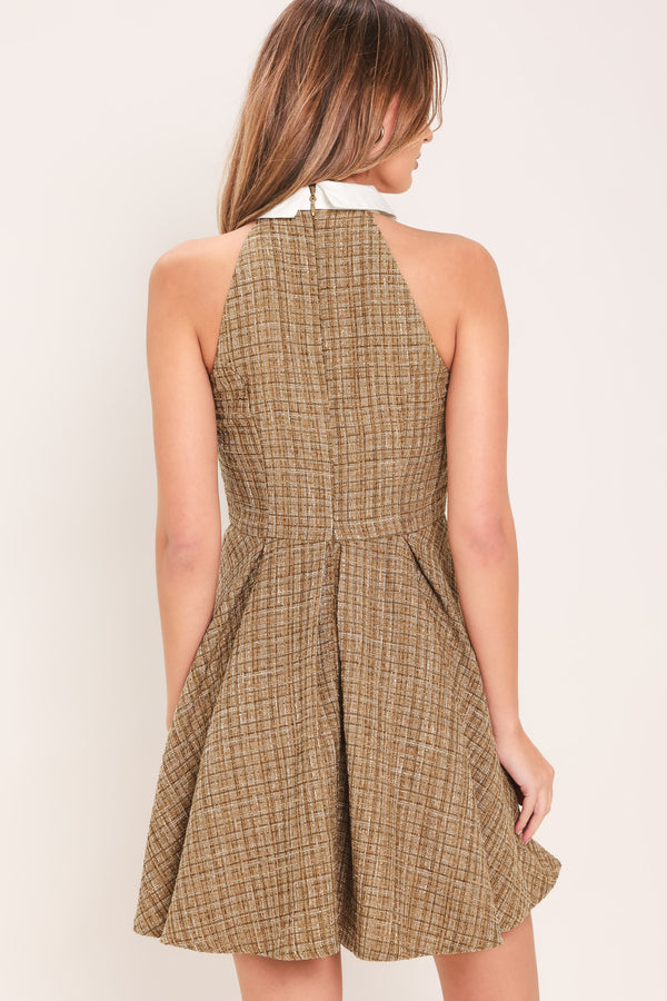 Woman wearing a hazel tweed mini dress featuring halter neckline with white collar finish, front button detail, full circle skirt and back zipper closure background | Flying Tomato