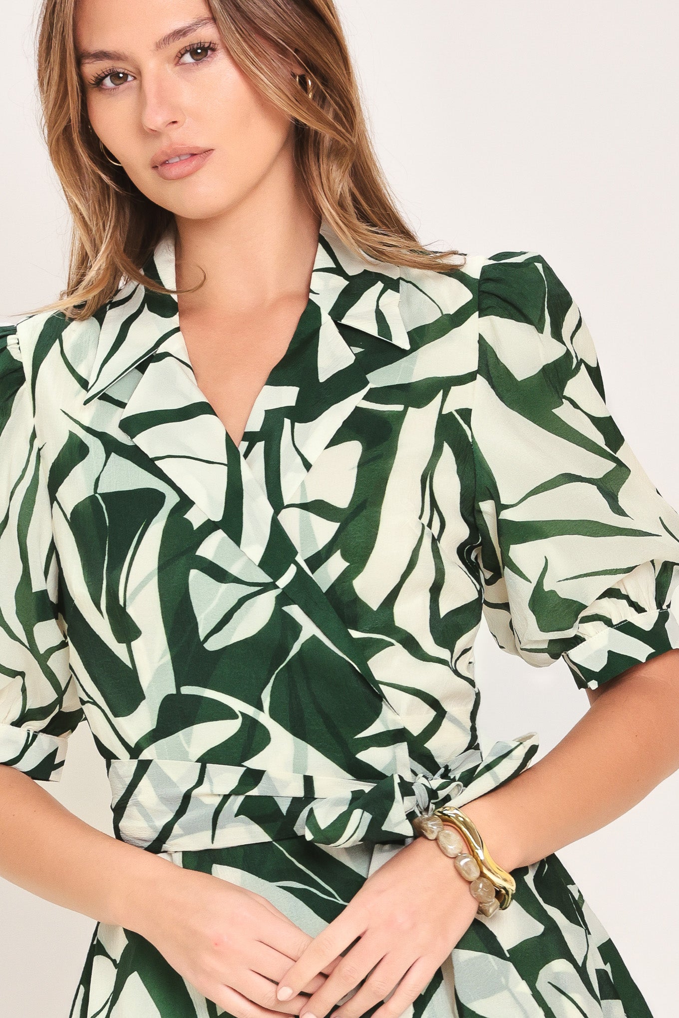 Woman wearing an green and ivory leaf-patterned true wrap midi dress featuring collar, puff short sleeve and full skirt | Flying Tomato