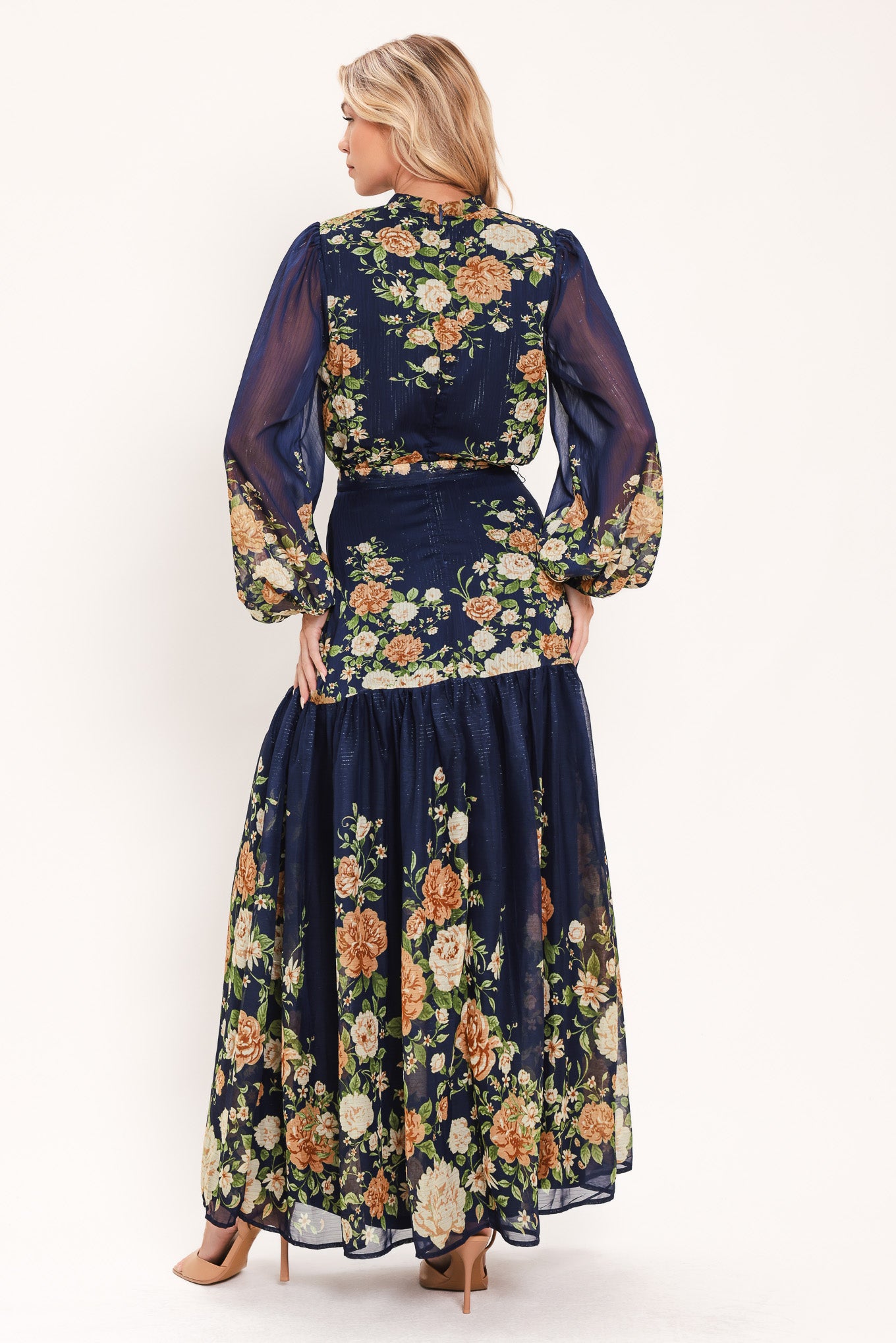 A woman modeling a navy blue long-sleeve maxi dress with a floral print. The dress features a tie-neck detail, a matching waist tie, and a tiered skirt | Flying Tomato