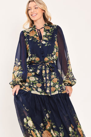 A woman modeling a navy blue long-sleeve maxi dress with a floral print. The dress features a tie-neck detail, a matching waist tie, and a tiered skirt | Flying Tomato