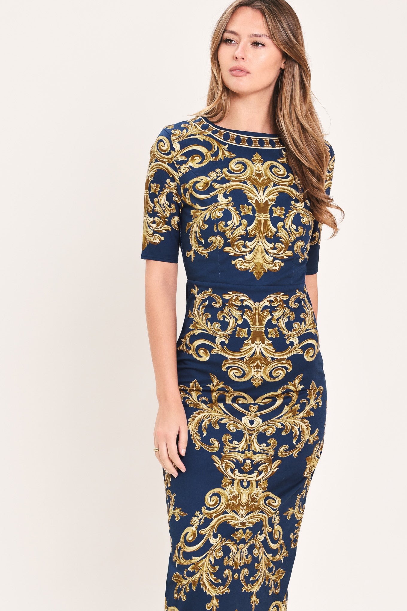 A woman wearing a navy blue midi dress with an ornate gold baroque pattern, featuring short sleeves and a crew neck | Flying Tomato