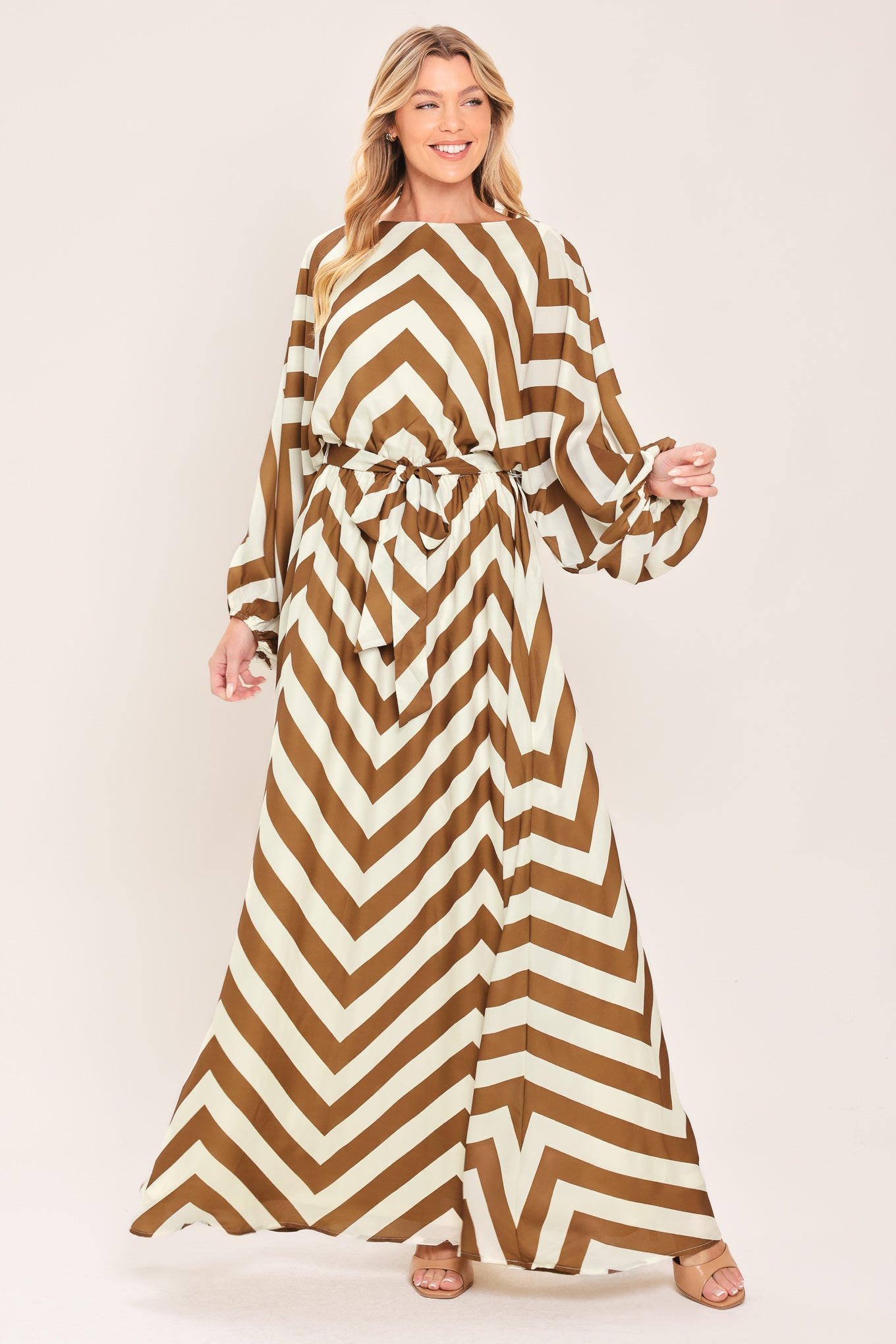 A woman modeling a long-sleeve maxi dress with a bold brown and ivory chevron pattern, featuring a tie waist belt | Flying Tomato