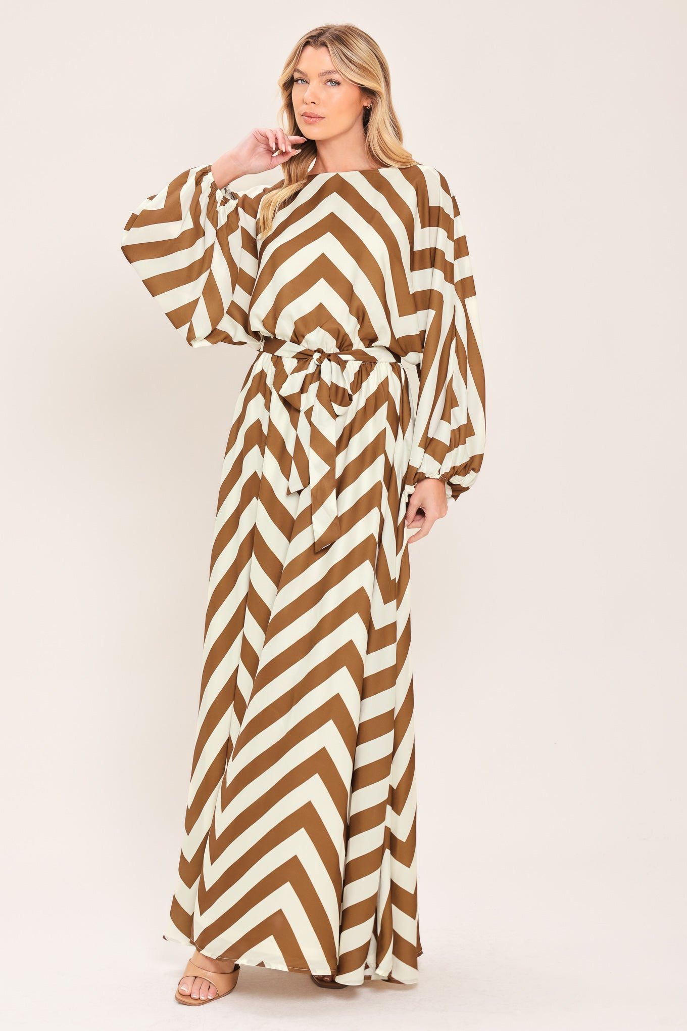 A woman modeling a long-sleeve maxi dress with a bold brown and ivory chevron pattern, featuring a tie waist belt | Flying Tomato