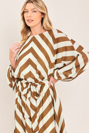 A woman modeling a long-sleeve maxi dress with a bold brown and ivory chevron pattern, featuring a tie waist belt | Flying Tomato