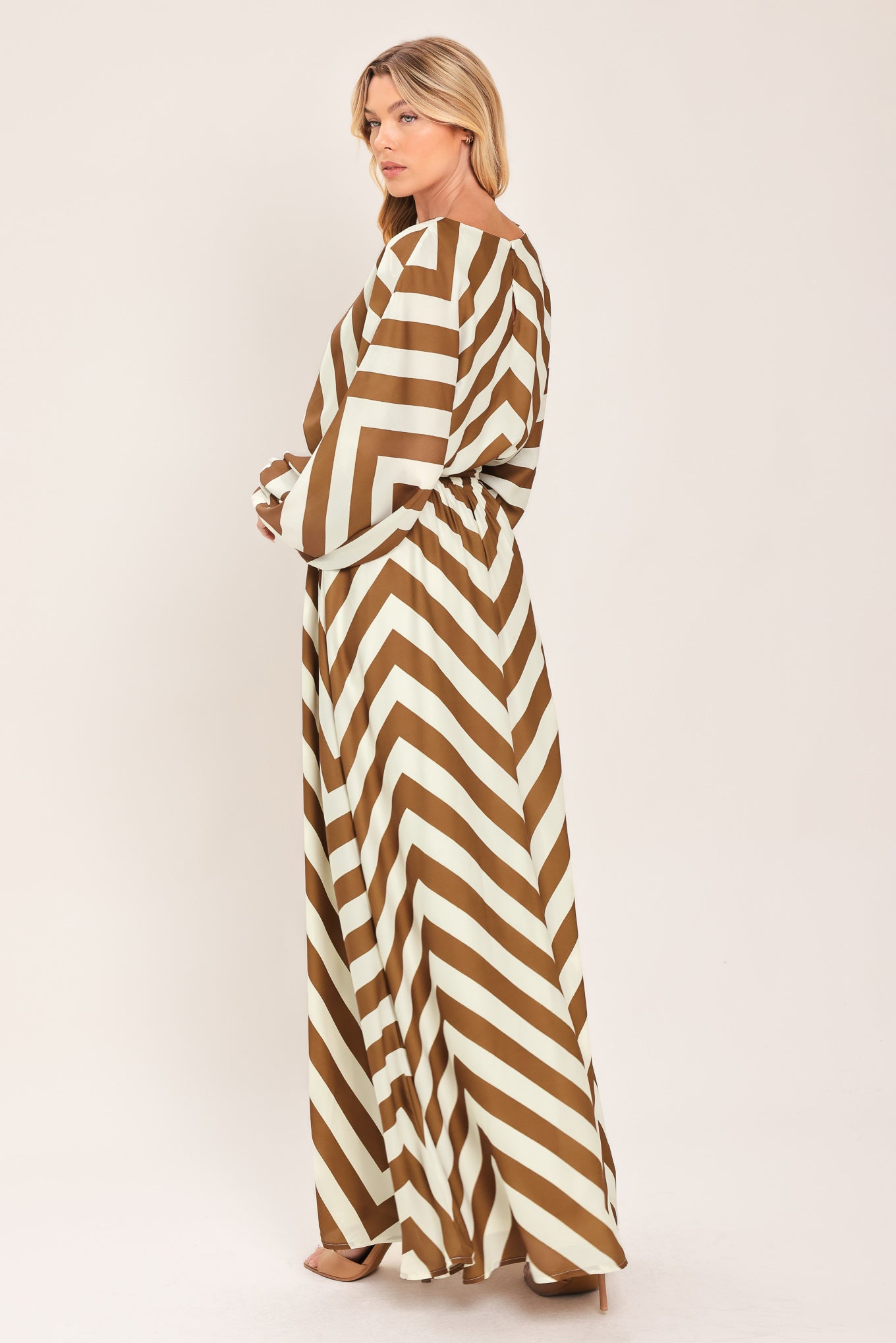 A woman modeling a long-sleeve maxi dress with a bold brown and ivory chevron pattern, featuring a tie waist belt | Flying Tomato