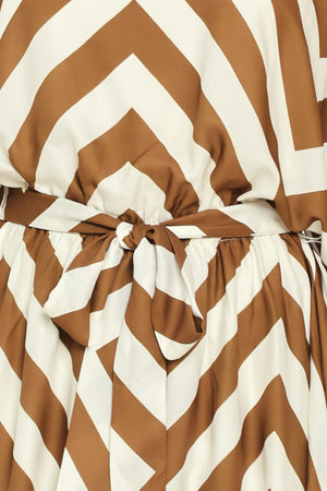 A woman modeling a long-sleeve maxi dress with a bold brown and ivory chevron pattern, featuring a tie waist belt | Flying Tomato