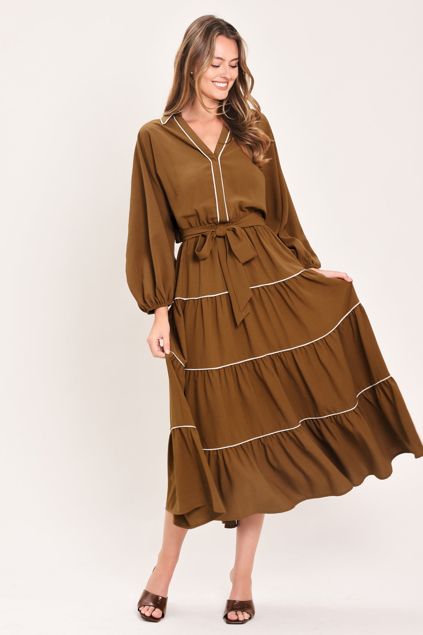 A woman wearing a brown long sleeve midi dress with white lined details, tiered skirt and self tie belt | Flying Tomato