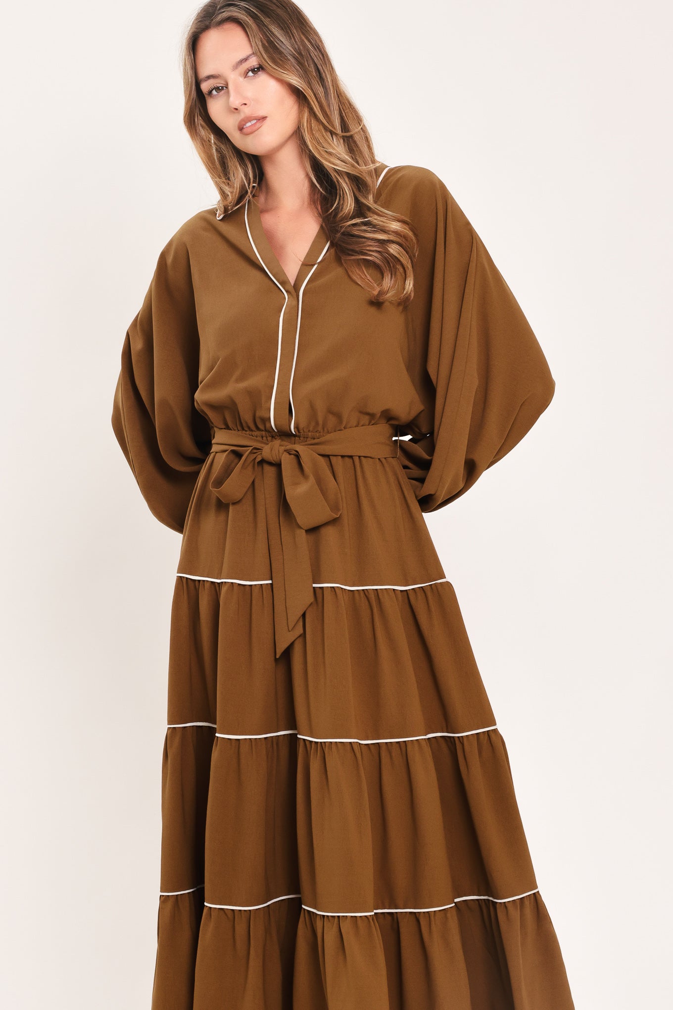 A woman wearing a brown long sleeve midi dress with white lined details, tiered skirt and self tie belt | Flying Tomato