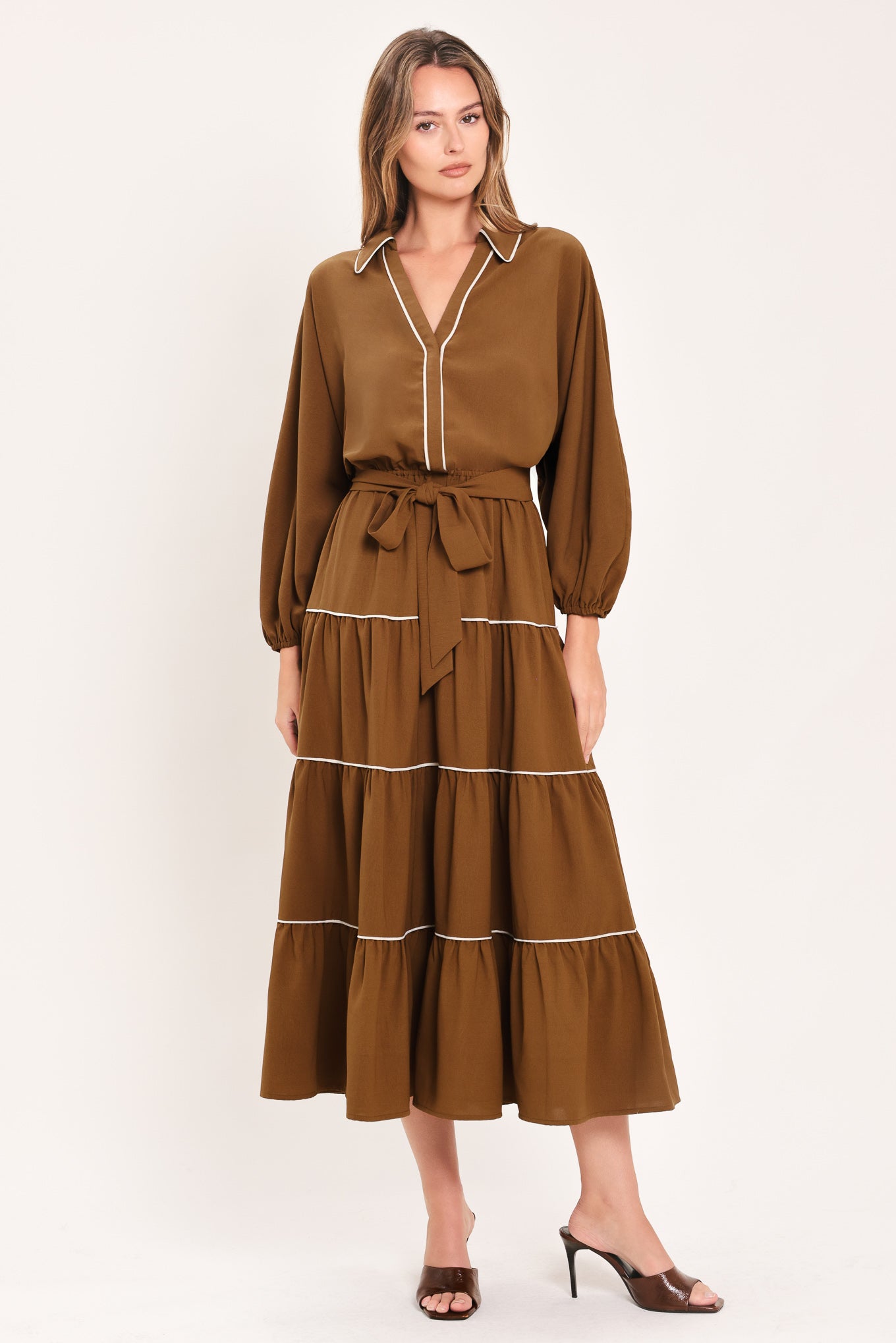 A woman wearing a brown long sleeve midi dress with white lined details, tiered skirt and self tie belt | Flying Tomato
